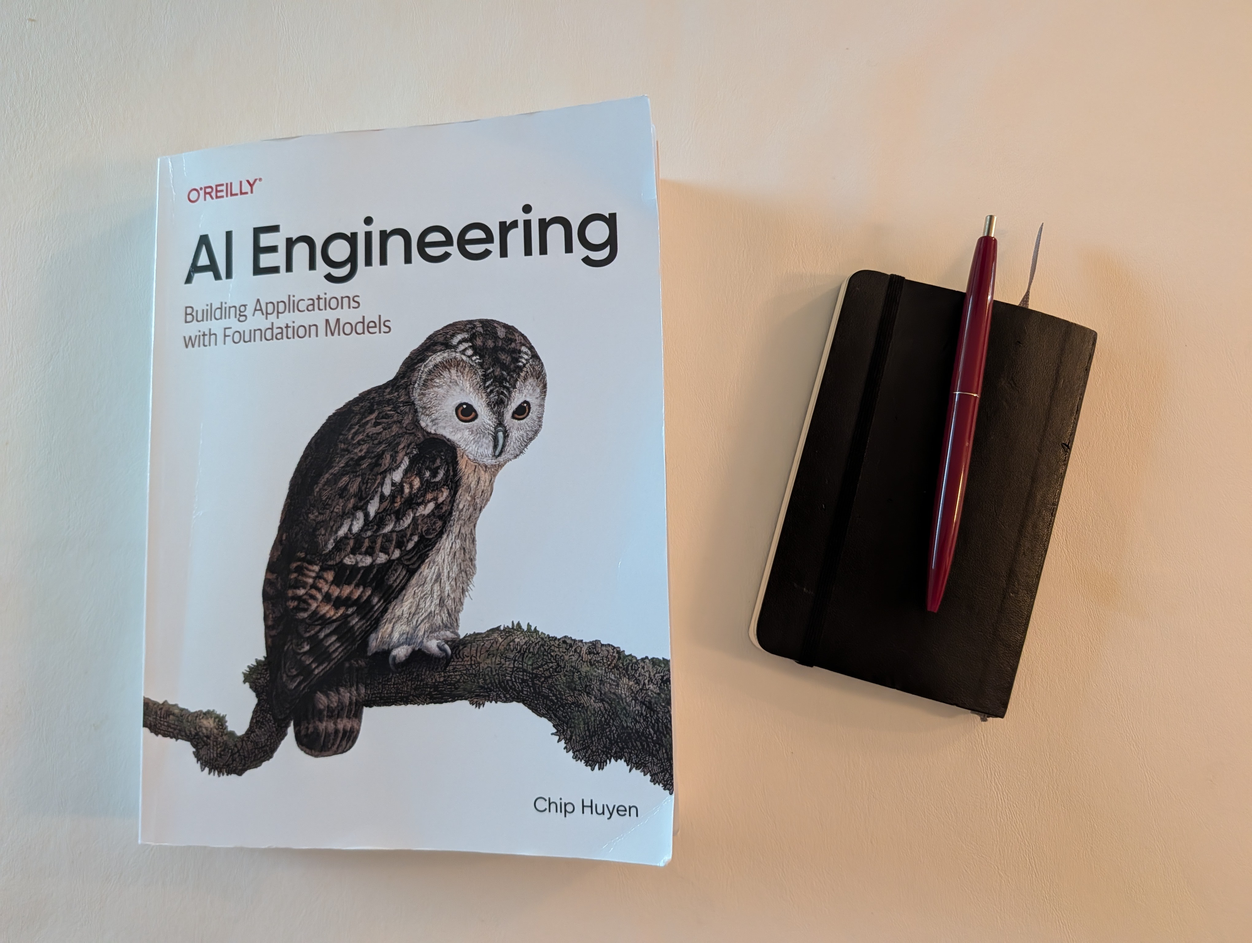 AI Engineering book by Chip Huyen next to a Moleskine notebook and pen